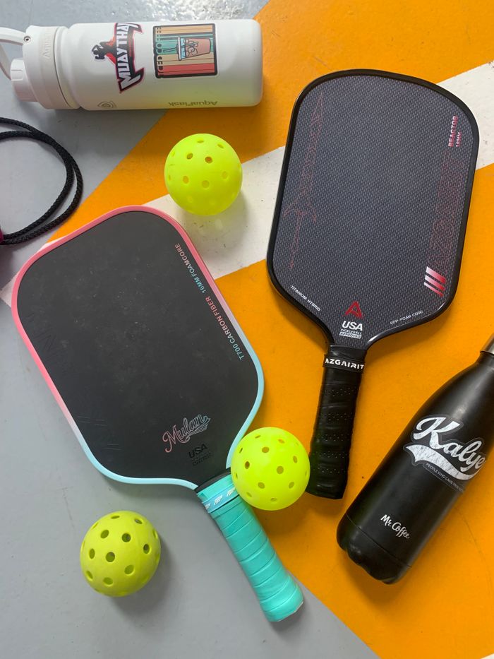 The Art of Drawing Readers In: Your attractive post title goes here Pickleball paddles and balls arranged with water bottles on a colorful floor.